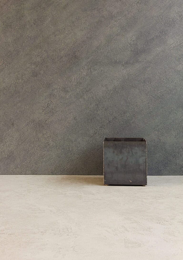 Dark grey sample cube on ErreLAB Pietra Continua Scisto textured wall with ErreLAB Travertino floor